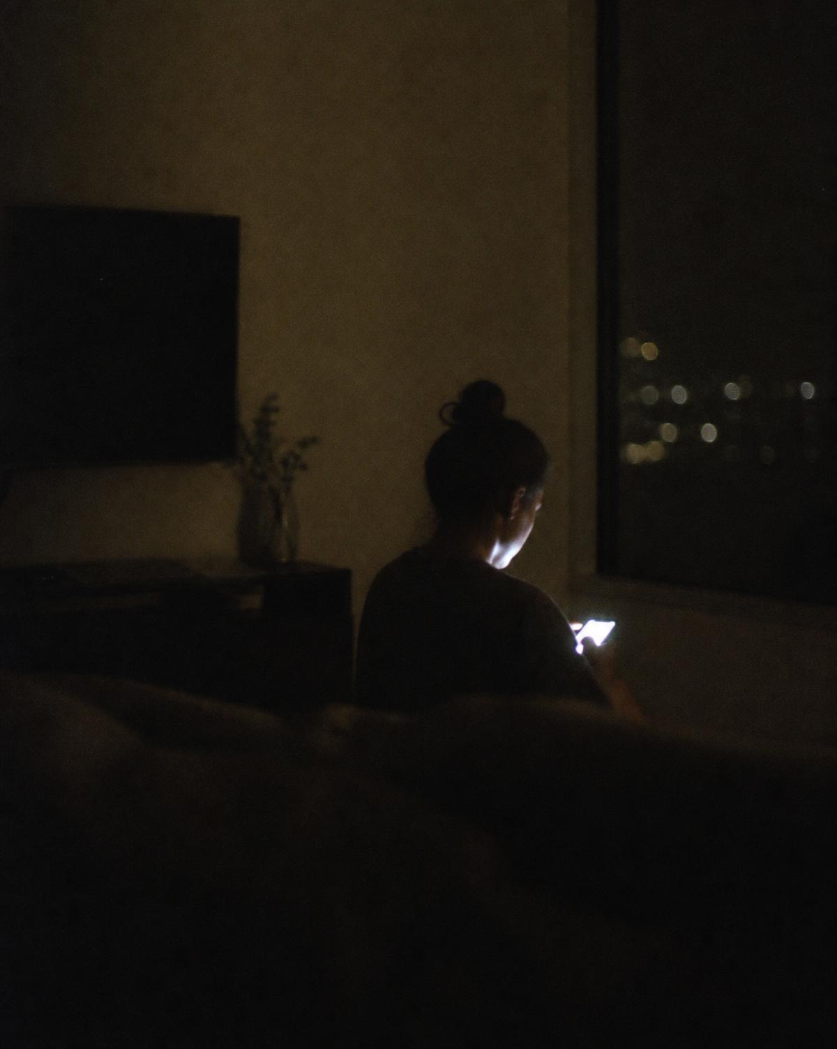 A person sitting in a dark room, their face lit by a phone screen